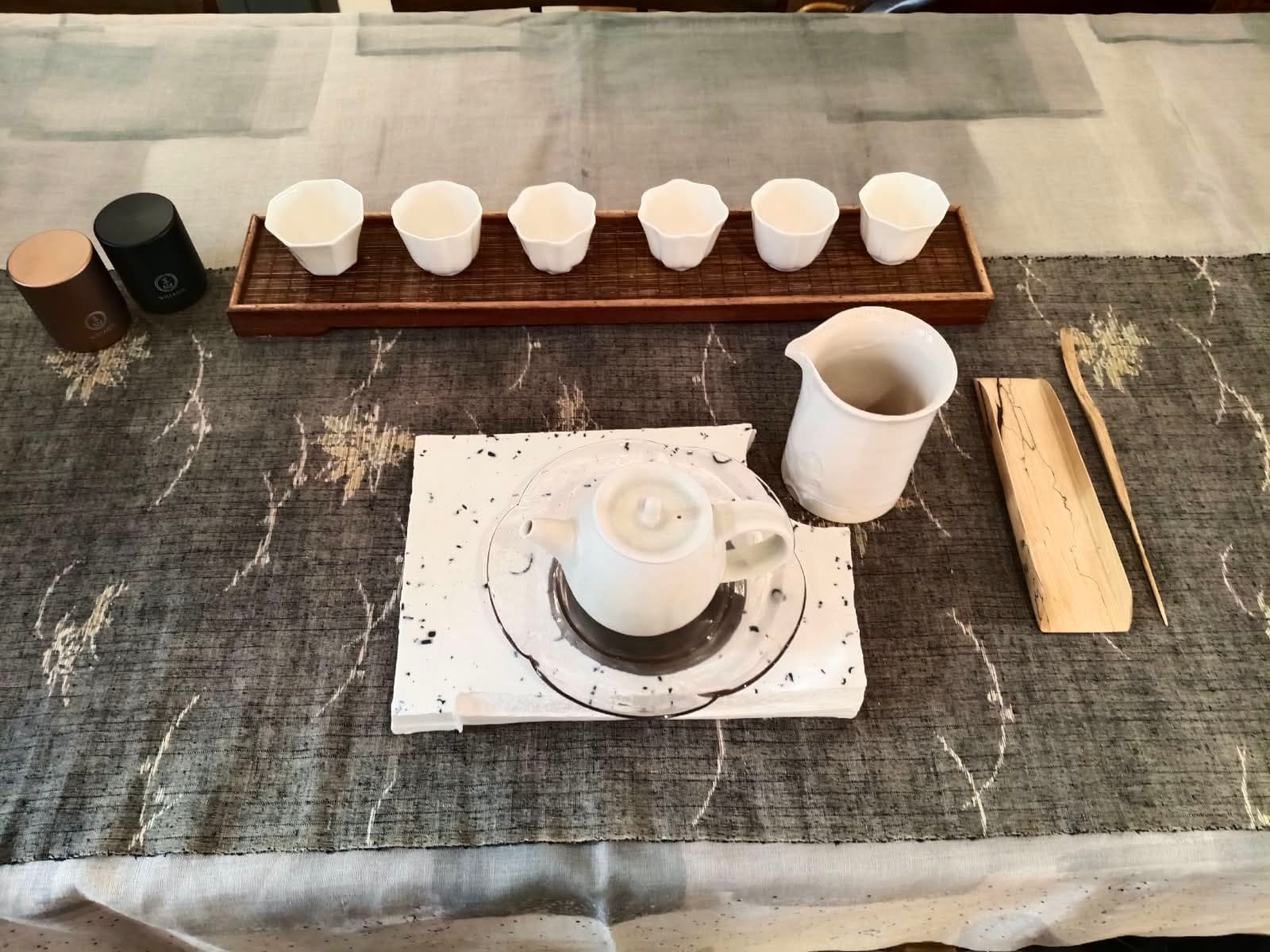 A Wistaria tea table: six porcelain cups, a white teapot and pitcher on a grey linen runner